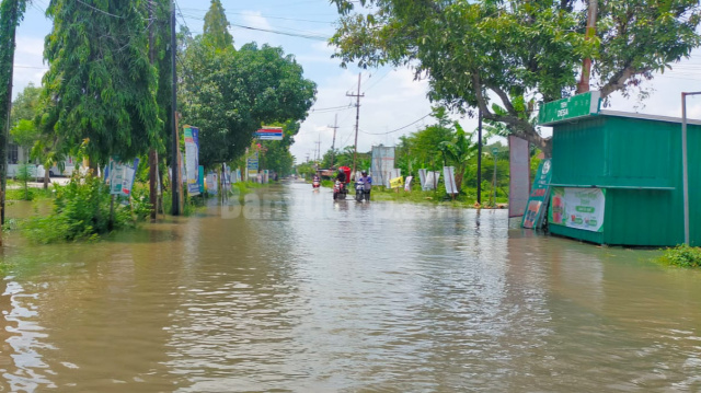 BENCANA ALAM : Pengendara sedang menuntun sepeda motornya karena jalan poros Desa Kalianyar tergenangi air.