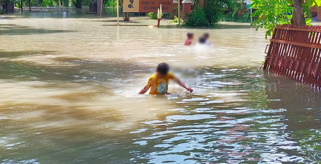 Anak-anak sedang bermain di halaman rumah yang terendam air.