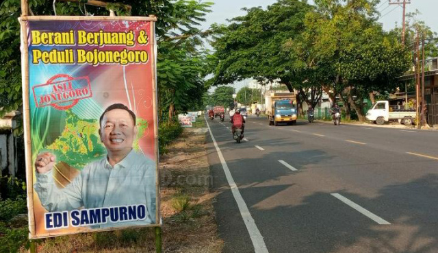 Banner bergambar Kades Campurejo Edi Sampurno terpasang di suatu titik tepi jalan nasional.